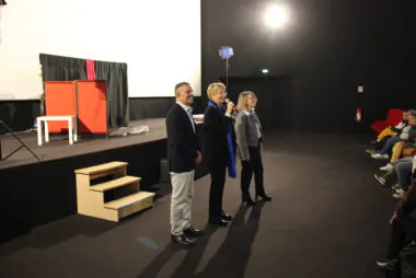 trois personnes au micro qui s'adressent à une salle de spectacle